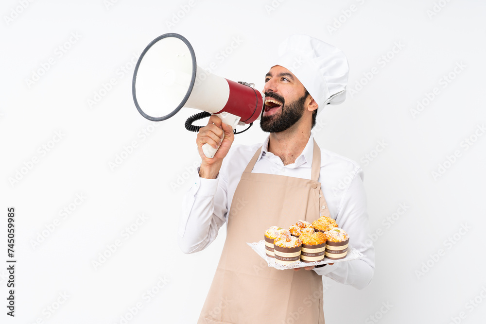 Wall mural Young man holding muffin cake over isolated white background shouting through a megaphone