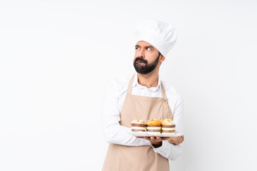 Young man holding muffin cake over isolated white background with confuse face expression