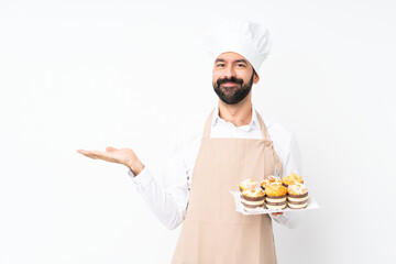 Young man holding muffin cake over isolated white background holding copyspace imaginary on the palm to insert an ad