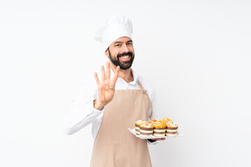 Young man holding muffin cake over isolated white background happy and counting four with fingers