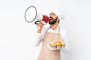 Young man holding muffin cake over isolated white background shouting through a megaphone