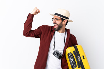 Traveler man man with beard holding a suitcase over isolated white background celebrating a victory