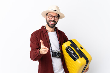 Traveler man man with beard holding a suitcase over isolated white background shaking hands for...