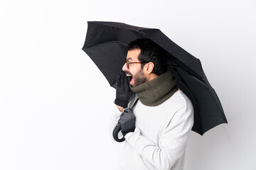 Caucasian handsome man with beard holding an umbrella over isolated white wall shouting with mouth wide open to the lateral