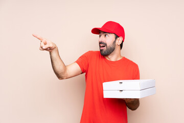Young man holding a pizza over isolated background pointing away