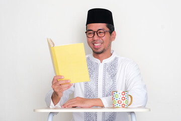 Moslem Asian man reading a book with happy expression - obrazy, fototapety, plakaty