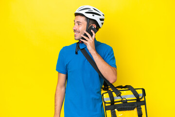 Young handsome man with thermal backpack over isolated yellow background keeping a conversation...