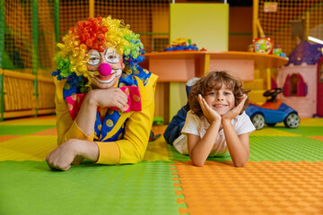 Portrait of happy smiling clown and little boy child lying on floor