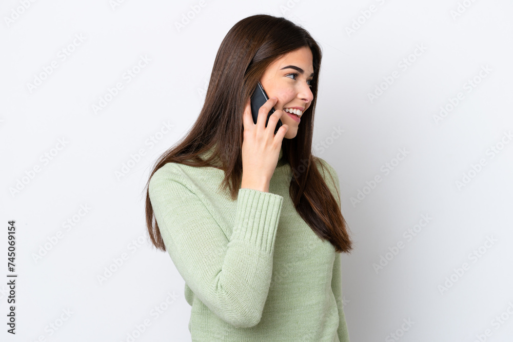 Wall mural Young Brazilian woman isolated on white background keeping a conversation with the mobile phone with someone