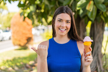 Young pretty Brazilian woman with a cornet ice cream at outdoors pointing to the side to present a...