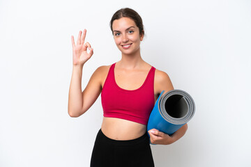 Young sport caucasian woman going to yoga classes while holding a mat isolated on white background showing ok sign with fingers