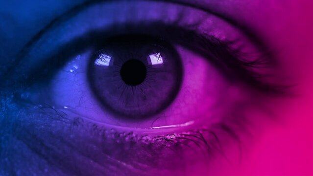 Close up shot of macro eye opening and blinking in Pink-blue-green color light. Female pink eye in neon lights. Macro look of the human eye. 