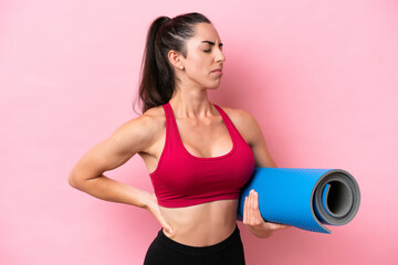 Young sport caucasian woman going to yoga classes while holding a mat isolated on pink background suffering from backache for having made an effort