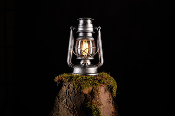 Vintage Kerosin Lampe mit LED isoliert auf einem Baumstamm mit Moos vor dunklen Hintergrund....