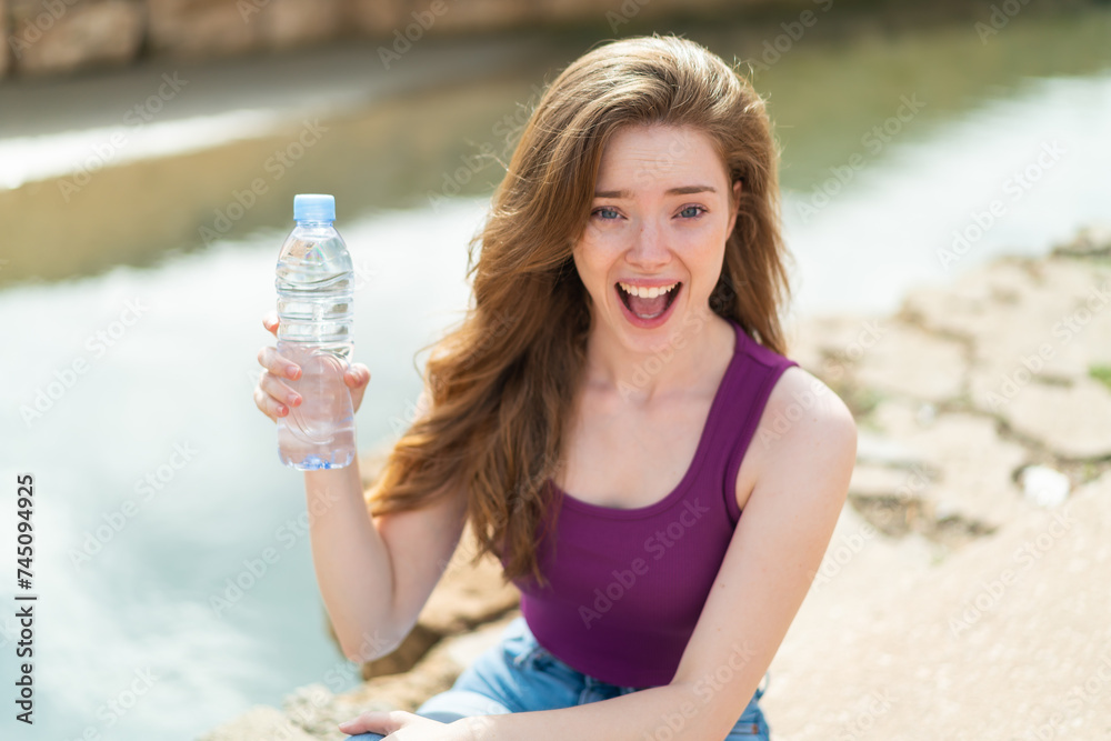 Sticker Young redhead woman with a bottle of water at outdoors with surprise and shocked facial expression