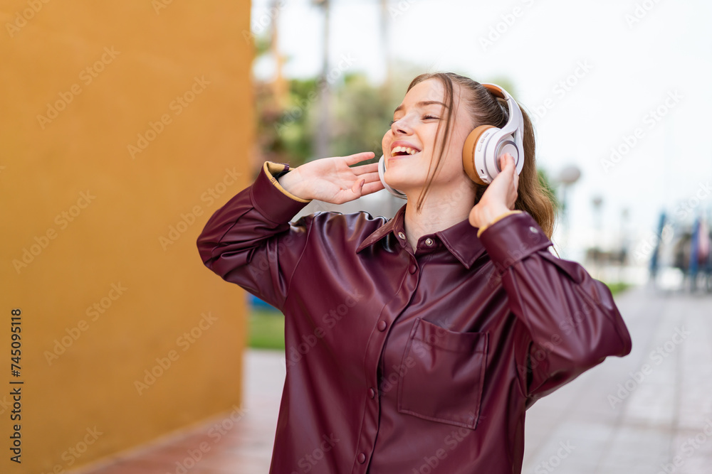 Wall mural Young pretty girl at outdoors listening music and singing