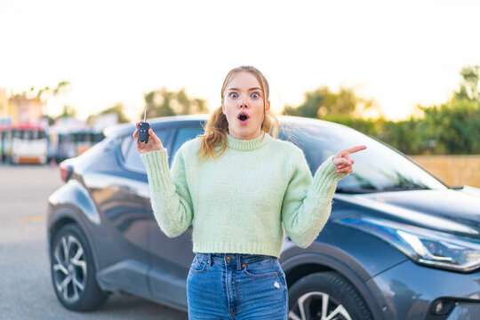 Young pretty girl holding car keys at outdoors surprised and pointing side