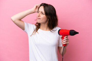 Young caucasian woman holding a hairdryer isolated on pink background having doubts and with confuse face expression