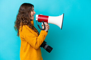 Young photographer woman isolated on blue background shouting through a megaphone