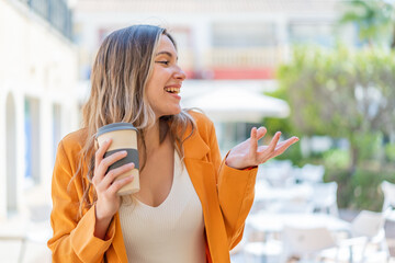 Young pretty woman holding a take away coffee at outdoors with surprise facial expression