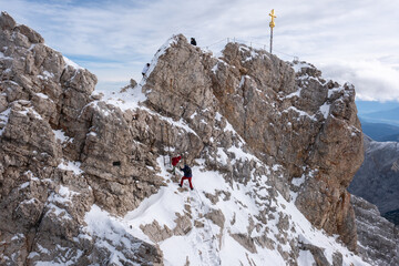 Hikers ascending the rocky, snow-capped summit of the Zugspitze, the tallest mountain in the German...