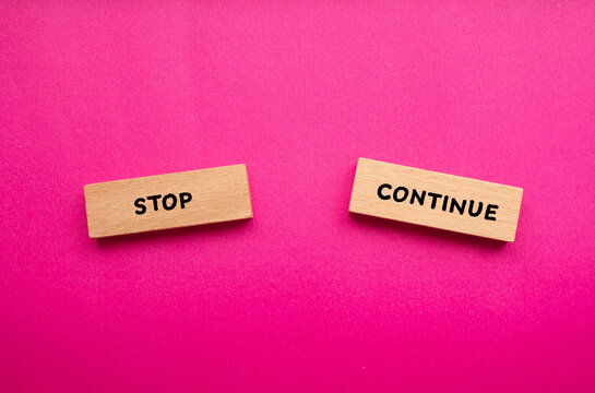 Stop or continue words written on wooden blocks with pink background. Conceptual symbol. Copy space.