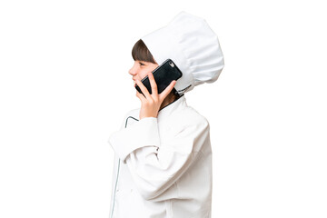 Little caucasian chef girl over isolated background keeping a conversation with the mobile phone with someone