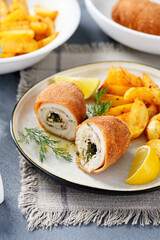 Chicken Kiev breast stuffed with butter, garlic and dill. Served with baked potato slices and fresh herbs.