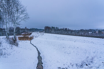 railway tracks with a bend to the right and a brook nearby in winter