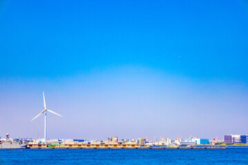 青空の横浜みなとみらいにそびえ立つ風力発電の風車と倉庫と工場・海の景色（神奈川県横浜市）