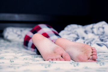 Bare feet of a child in pajamas. The child sleeps on the bed with bare feet. Legs and feet. Heel