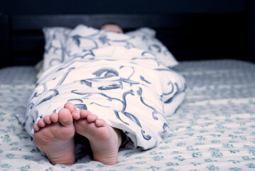 Bare feet of a child. The child's legs look out from under the blanket. Foot and leg