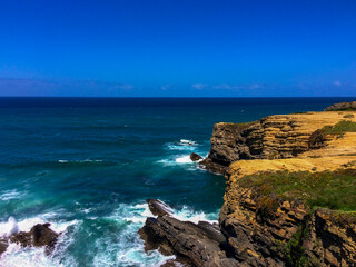Fototapeta na wymiar A rocky coastline with waves crashing, under a clear blue sky.