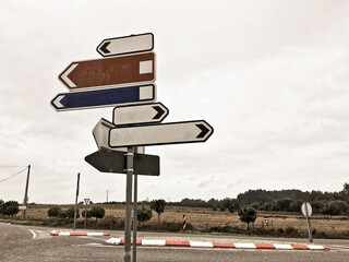 A signpost with five blank directional arrows at a road intersection, under a cloudy sky.