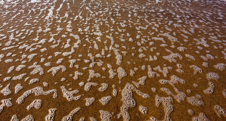 The image captures a sandy surface with irregular white foam patterns, likely left by receding waves.