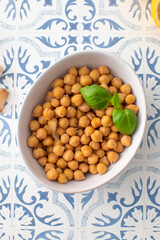 Canned chickpeas in a bowl with a basil leaf on the table. Vegetable protein.