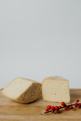 Two pieces of cheese are displayed on a wooden cutting board, accompanied by red berries. This food pairing enhances the dishs sweetness and complements the overall presentation