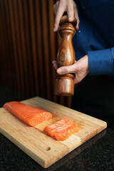 Chief hands salting salmon fillet on wooden table at kitchen