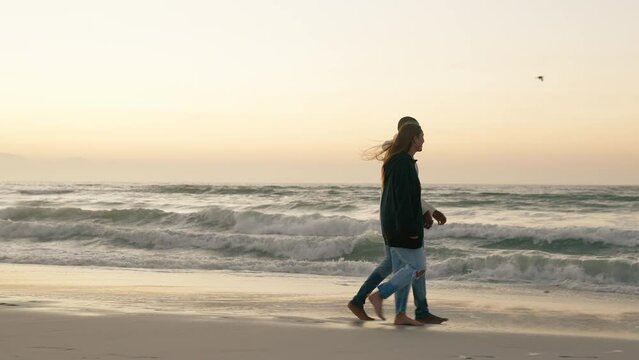 Casually Dressed Loving Young Couple Walking Along Beach Shoreline Holding Hands At Sunrise