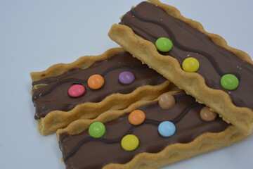 Sweets, delicious, interesting desserts, cookies with caramel, milk chocolate and small colored candies arranged on a white background.