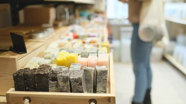 Woman chooses organic cosmetic products in zero waste beauty shop. Focus on organic soap. Woman buying beauty products in plastic free organic cosmetics store