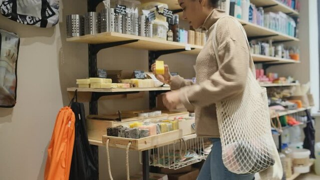 Young African American woman chooses organic cosmetic products in zero waste beauty shop. Woman buying soap in sustainable organic cosmetics store