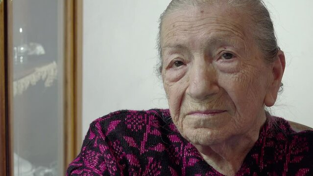 Portrait of a very Old Woman turning her gaze to the camera sitting at home