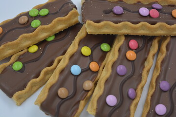 Sweets, delicious, interesting desserts, cookies with caramel, milk chocolate and small colored candies arranged on a white background.