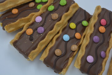 Sweets, delicious, interesting desserts, cookies with caramel, milk chocolate and small colored candies arranged on a white background.