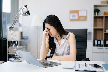 Obraz na płótnie Canvas Asian woman feeling migraine head strain.Overworked businesswoman financier while working on laptop.