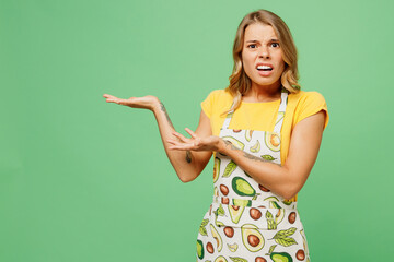 Young sad dissatisfied mad housewife housekeeper chef cook baker woman she wear apron yellow t-shirt point hands aside on area isolated on plain pastel green background studio. Cooking food concept.