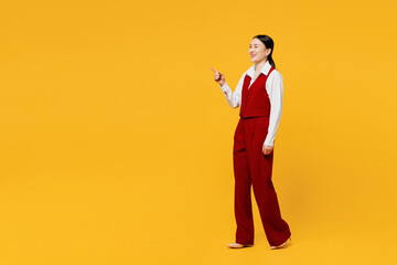 Full body side view young happy lawyer employee business woman of Asian ethnicity wear formal red vest shirt work at office point index finger aside on area isolated on plain yellow background studio.
