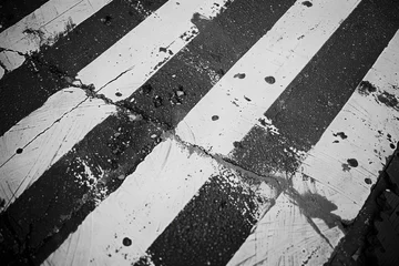 Foto op Plexiglas A worn zebra crossing on an asphalt street showing signs of use and weathering. © Sandris