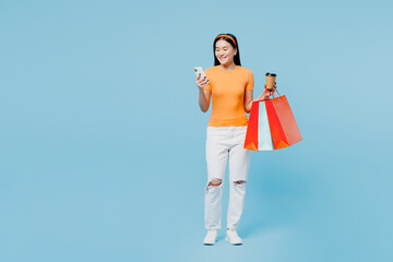 Full body fun young woman wears orange t-shirt casual clothes hold in hand paper package bags after...